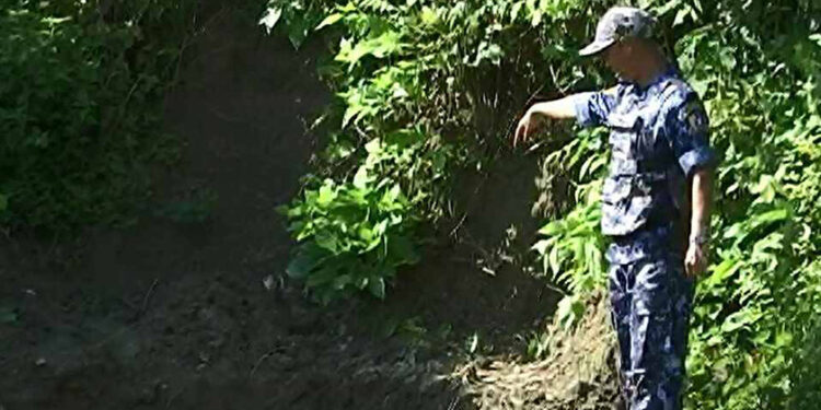 A member of the security forces stands near a pit where Hindu bodies were found on Sunday. / Supplied