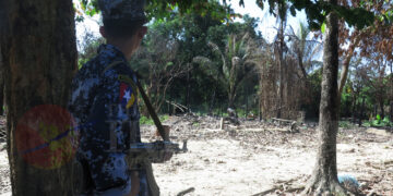 A border policeman stands in Wa Piek, a Muslim village located near a police outpost in Maungdaw Township. It has been burned down. / Moe Myint / The Irrawaddy