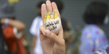An anti-coup protester raises a decorated Easter egg along with the three-fingered symbol of resistance during a protest against the military coup on April 4, 2021 in Yangon. / AP