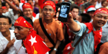 A man brandishes a phone with a picture of opposition leader Daw Aung San Suu Kyi, as election results are revealed on a screen in front of the Yangon head office of the National League for Democracy, April 1, 2012. / Reuters