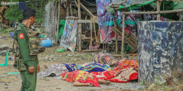 A Myanmar Army soldier looks at the covered bodies of those killed during an attack by an alliance of ethnic armed groups near Goke Twin Bridge in northern Shan State on Thursday. / Zaw Zaw / The Irrawaddy