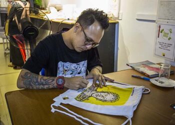 Artist Kyar Pauk signs a bag bearing a print of one of his paintings for a visitor on the opening day of his second solo exhibition, 'Micro', at the We Creation gallery on July 1. / Htet Wai