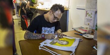Artist Kyar Pauk signs a bag bearing a print of one of his paintings for a visitor on the opening day of his second solo exhibition, 'Micro', at the We Creation gallery on July 1. / Htet Wai