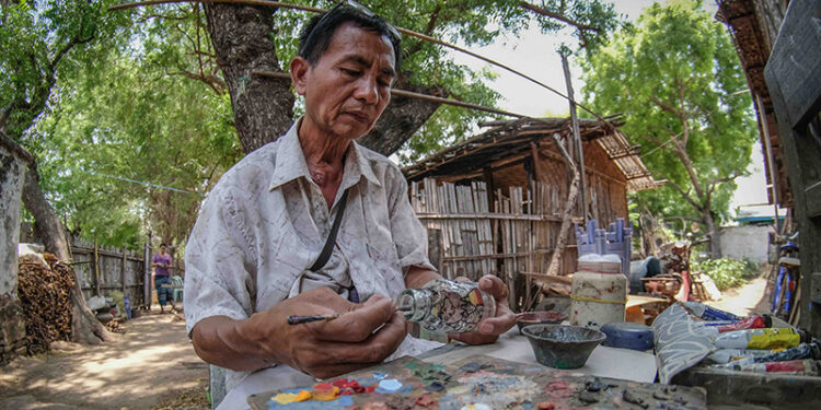 Artist Yaw Na Than paints a bottle at his home in Bagan. / Zaw Zaw / The Irrawaddy