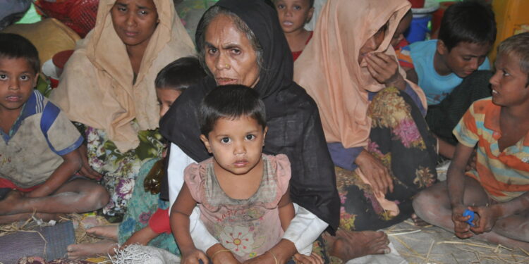 Rohingya women and children—displaced from Dar GyeeZar village—watch as authorities carry out relief efforts near Abujara village in northern Maungdaw Township. / Moe Myint / The Irrawaddy