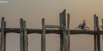 A  woman wearing a mask pedals her bicycle across the U Pain wooden bridge. / Zaw Zaw / The Irrawaddy