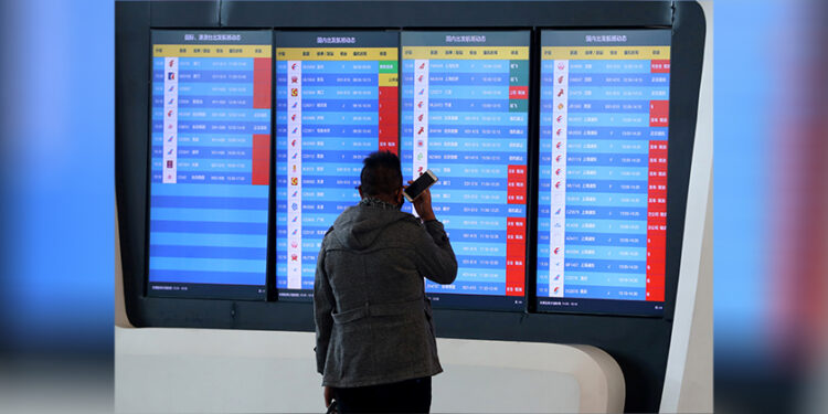 A man stands in front of a screen showing multiple flight cancellations at the airport in Wuhan, China on Jan. 23, 2020. / REUTERS