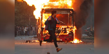 A man runs past a burning bus that was set on fire by demonstrators during a protest against a new citizenship law in New Delhi, India, on Dec 15, 2019. / REUTERS