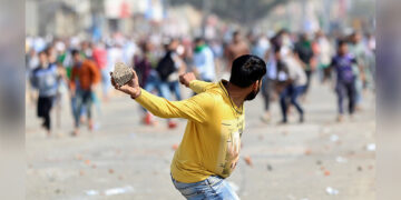 A man supporting a new citizenship law throws a stone at opponents of the law, during a clash in New Delhi on Feb. 24. / REUTERS