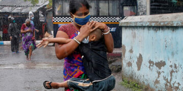 A woman tries to protect her son from heavy rain as they evacuate a slum in Kolkata, India during the approach of Cyclone Amphan on May 20, 2020. / Reuters