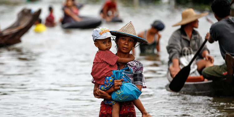 A woman carries her child as she walks through a flooded road in Kyaung Kone in Irrawaddy Region, Myanmar, August 12, 2016. / Soe Zayar Tun / Reuters
