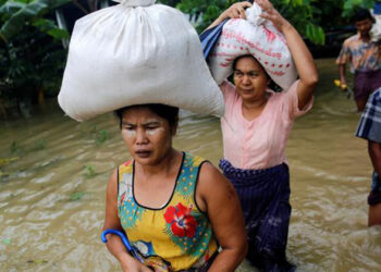 Women carry bags of rice after collecting them from donors in Irrawaddy Region, Myanmar, Aug. 12, 2016. / Reuters
