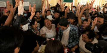 Funeral goers flash three-finger salutes of defiance as a mother mourns over her son who was killed by the regime's troops in Yangon in March. / The Irrawaddy