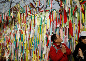 Tourists pose for photographs near a military fence decorated with ribbons bearing messages wishing for reunification near the demilitarized zone separating the two Koreas in Paju in February 2019. / Reuters