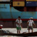 Two fishermen stand on a boat in front of an industrial port terminal on the banks of the Hlaing River in Yangon, June 9, 2016. / Reuters